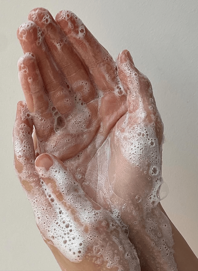 Mains savonneuses recouvertes de mousse, illustrant un geste de nettoyage doux et naturel pour entretenir sa literie et préserver un environnement de sommeil sain.