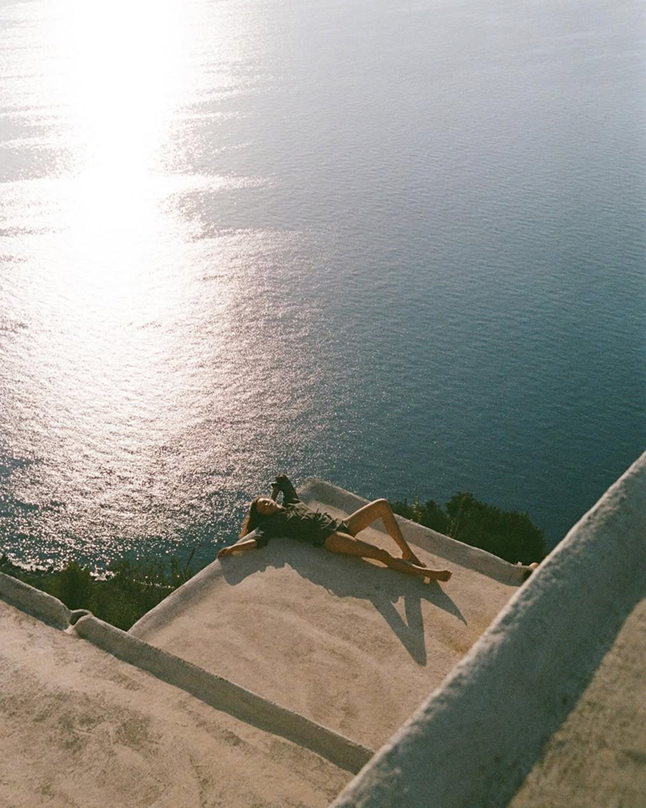 Donna sdraiata al sole di fronte al mare, che incarna un momento di relax e benessere immersi nella natura, simbolo di uno stile di vita sereno e rigenerante.