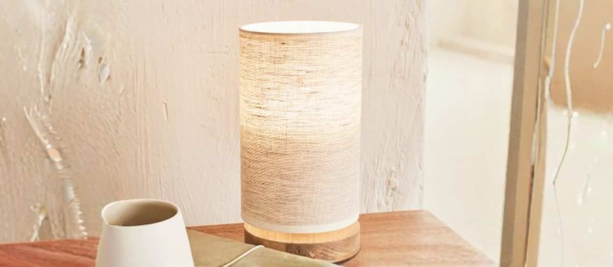 Lampada da tavolo in lino Kipli che diffonde una luce naturale su un comodino in legno in una camera da letto minimalista.