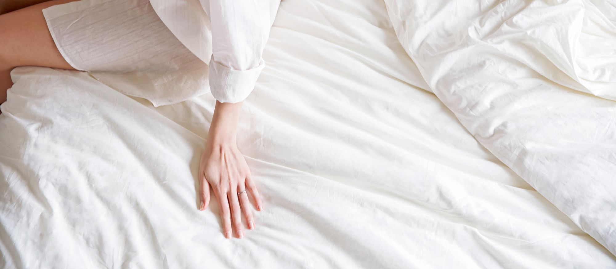 Una mano appoggiata su un lenzuolo di cotone biologico bianco, a sottolineare la morbidezza e la qualità del completo da letto Kipli.