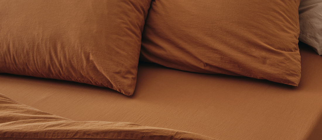 Bettwäsche aus Bio-Baumwolle in Terrakotta-Farbe auf einem Kipli-Bett – ein Beispiel für eine gemütliche Einrichtung und natürliche Textilien für ein gesundes Schlafzimmer.