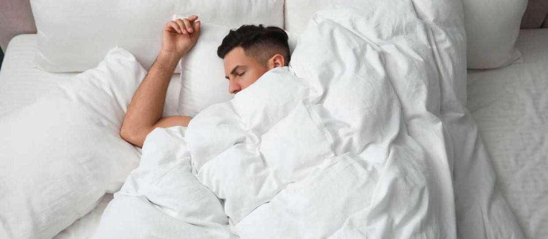 Ein Mann, der tief und fest in einem kuscheligen Bett schläft, was verdeutlicht, dass man im Winter mehr Schlaf braucht.