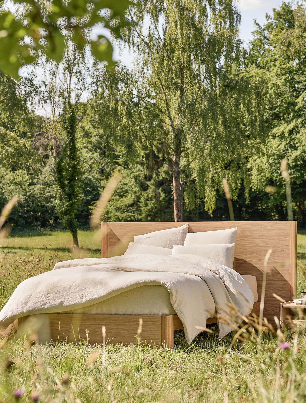 Lit en bois massif Kipli installé en pleine nature, avec linge de lit en matières naturelles, illustrant une chambre écoresponsable et un sommeil sain.