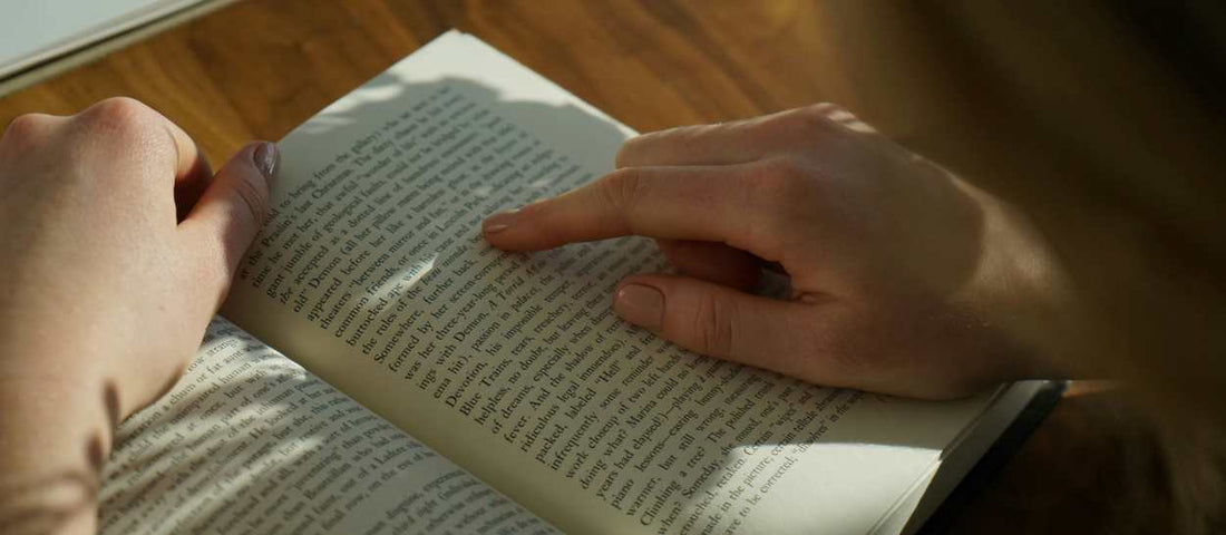 Nahaufnahme von Händen, die in einer von Tageslicht erhellten Leseecke in einem Buch blättern.