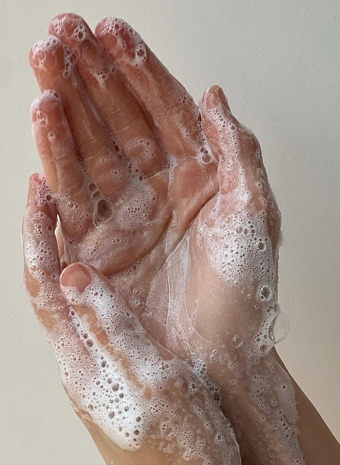 Mani insaponate e ricoperte di schiuma, che illustrano un gesto di pulizia delicato e naturale per prendersi cura della propria biancheria da letto e garantire un ambiente sano in cui dormire.